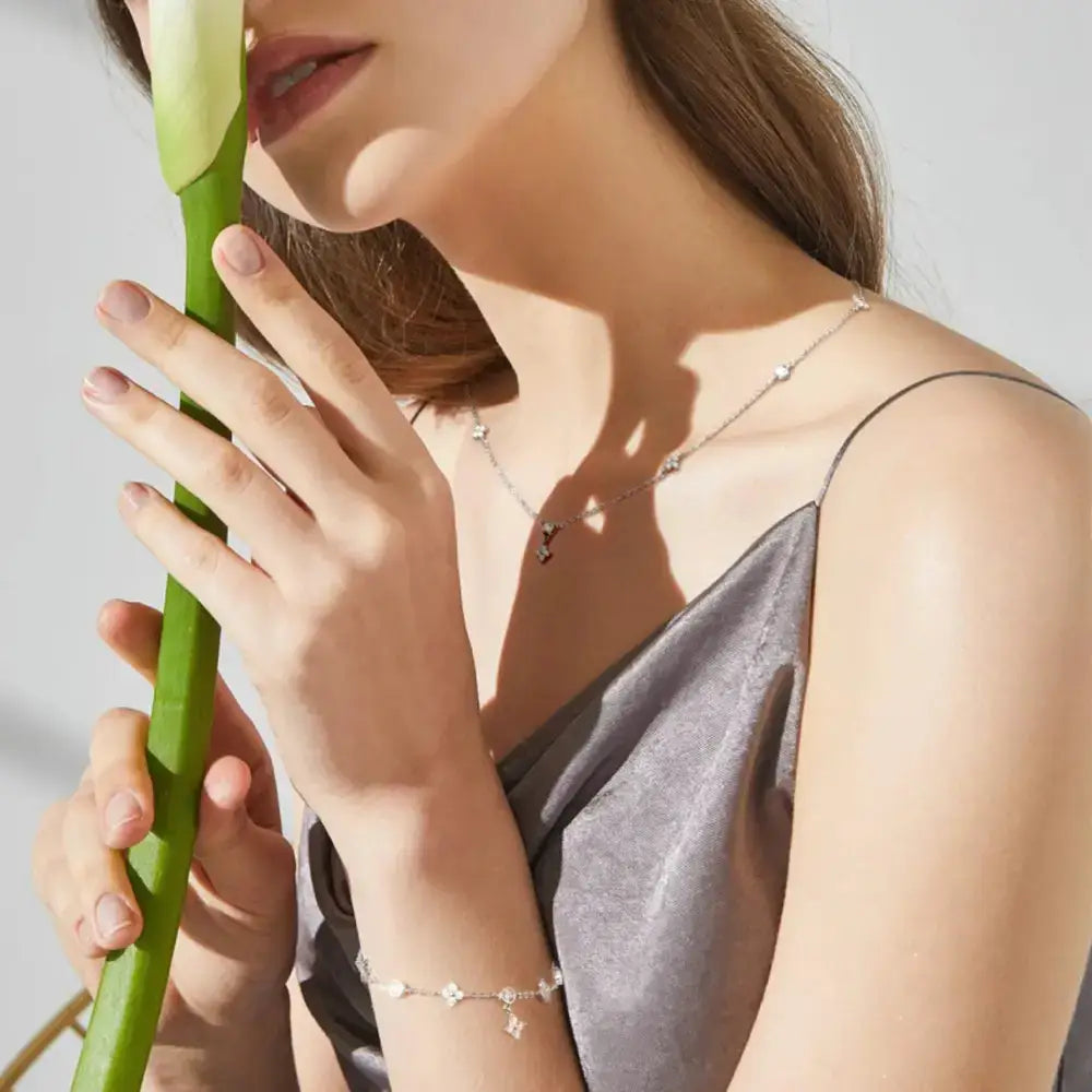 Person’s hand gently holding a green stem, showcasing Silver Four Leaf Clover Jewelry