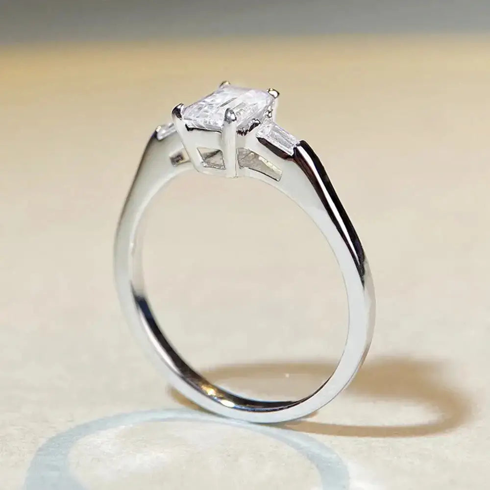 Silver engagement ring featuring an emerald cut moissanite diamond in a prong setting