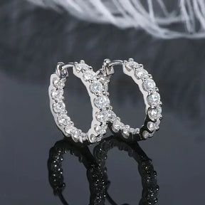 Pair of diamond-encrusted hoop earrings reflecting on dark surface, showcasing Sterling Silver Moissanite