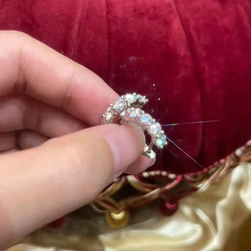 Diamond-studded ring held between fingers next to luxury lab grown diamond huggie earrings