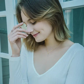 Woman with shoulder-length blonde hair wearing a white top and silver cross necklace